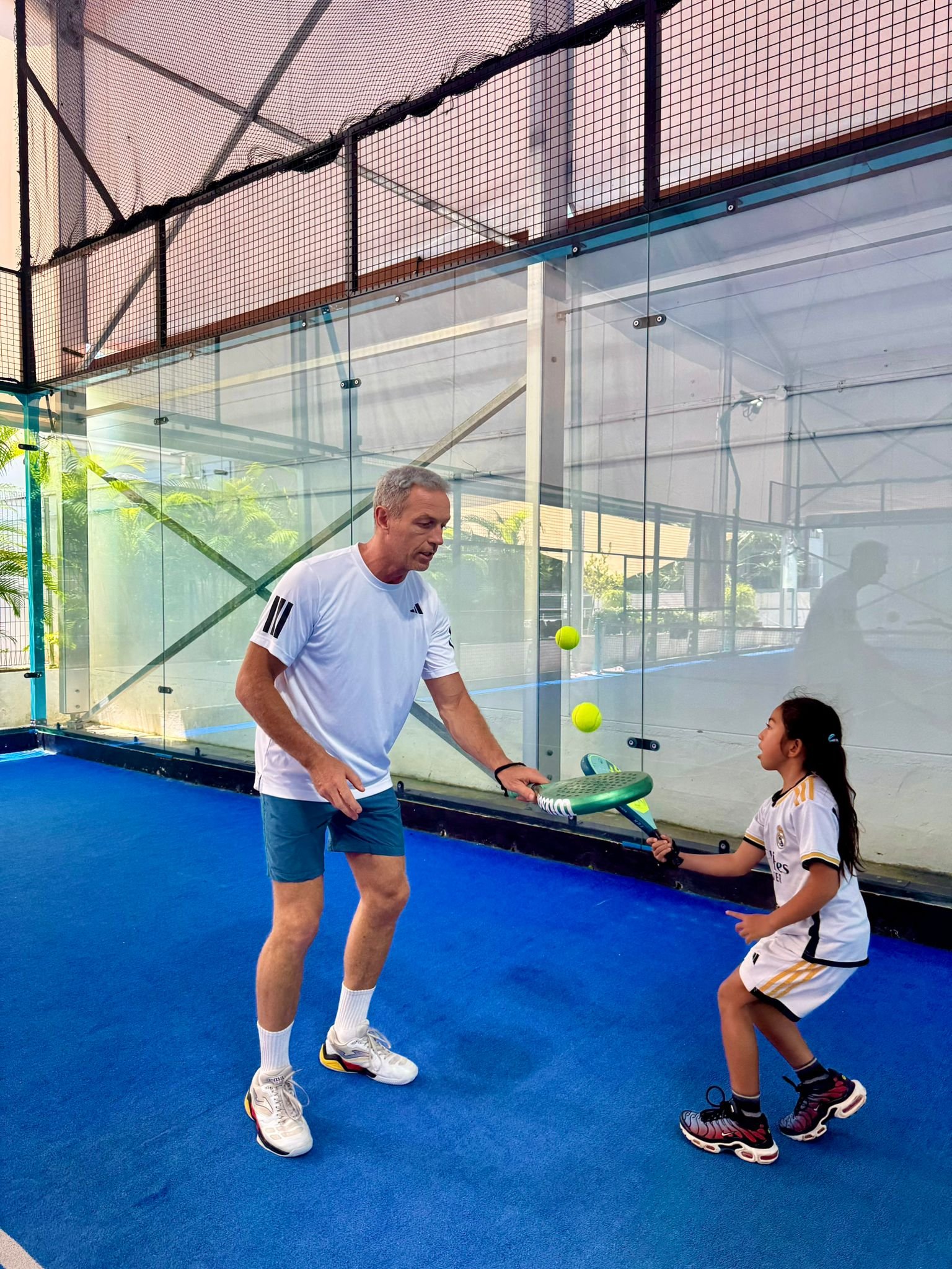 Young beginners practicing padel swings with coach guidance.
